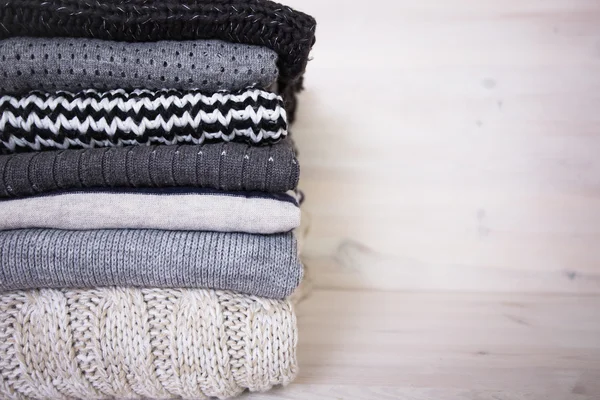 Stack of various woolen sweaters on a white wooden background — Stock Photo, Image