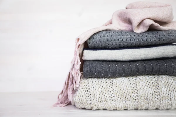 Stack of various woolen sweaters on a white wooden background — Stock Photo, Image