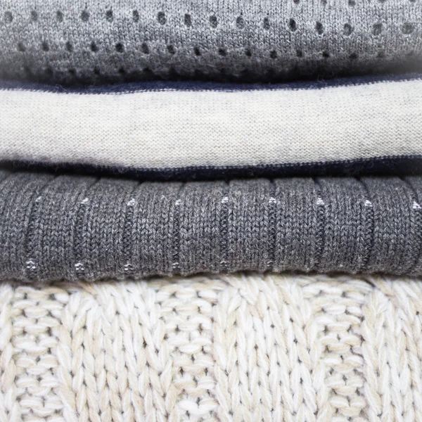 Pila di vari maglioni di lana su uno sfondo di legno bianco — Foto Stock