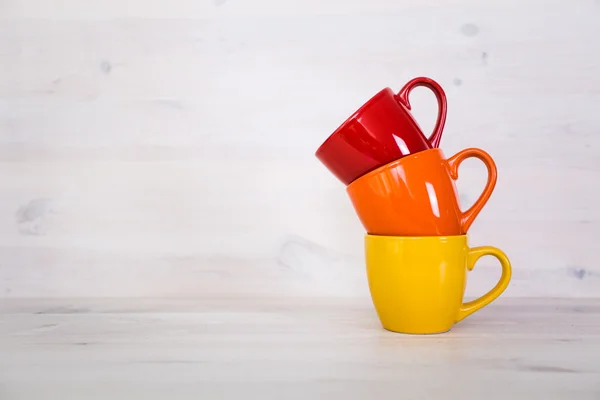 Pila di tazze di caffè colorate su uno sfondo di legno bianco — Foto Stock