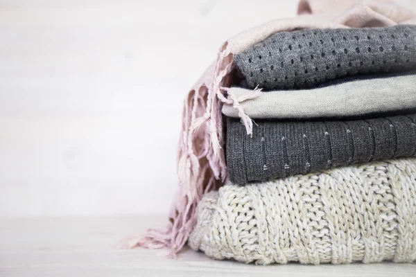 Stack of various woolen sweaters on a white wooden background — Stock Photo, Image