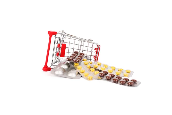 Pílulas e carrinho de compras em fundo branco — Fotografia de Stock
