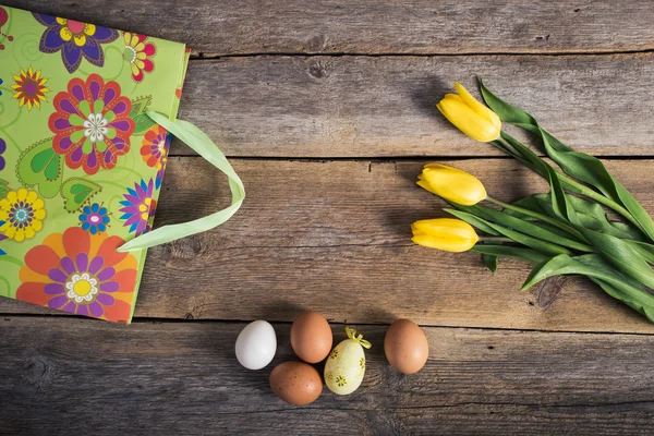 Тюльпаны и яйца с подарочными пакетами на деревянном фоне. Пасха — стоковое фото