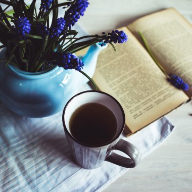 Bir fincan çay ile mavi çiçekler ve ahşap arka plan üzerine bir kitap. Vintage