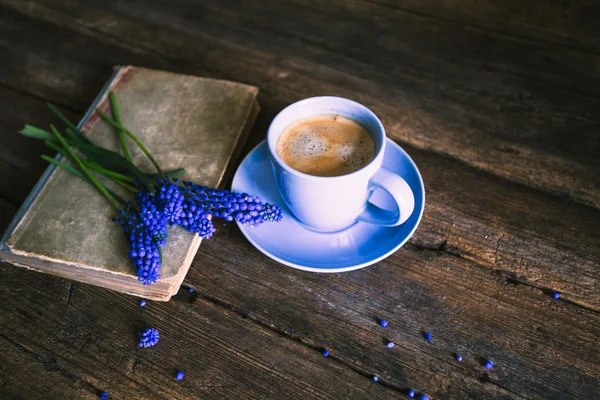 Flores azuis e uma xícara de café com um livro sobre um fundo de madeira — Fotografia de Stock