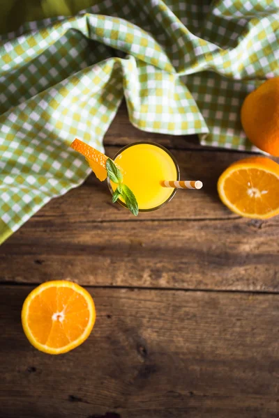 Апельсиновый сок в стакане с мятой, свежие фрукты на деревянном фоне — стоковое фото