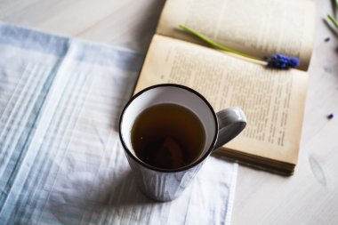 Mavi çiçekler ve ahşap arka plan üzerine bir kitap ile çay.