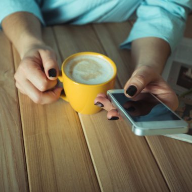 Kadın sarı Kupası elinde. Jel tırnak manikür. Telefon ve masanın üzerine dergi