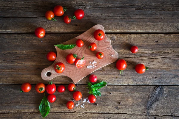 Fresh grape tomatoes with basil and coarse salt for use as cooking ingredients on kitchen board