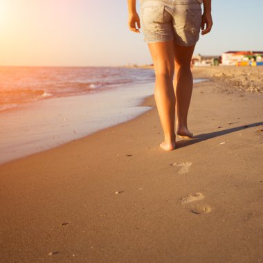 Gün batımında sahilde yürüyen bir kadın.