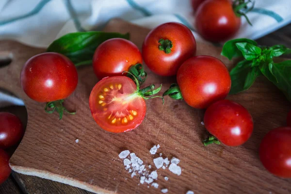 Fresh grape tomatoes with basil and coarse salt for use as cooking ingredients on kitchen board