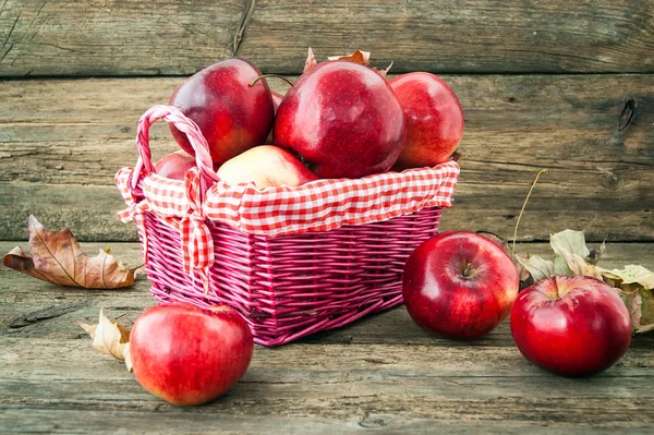 Červená jablka do koše na dřevěné pozadí — Stock fotografie