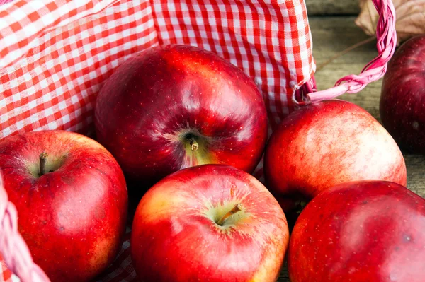 Červená jablka do koše na dřevěné pozadí — Stock fotografie