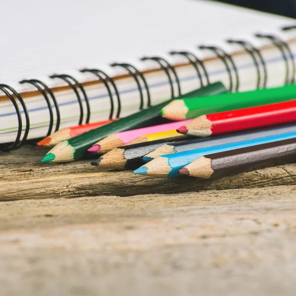 Carnet vierge vérifié avec crayons multicolores sur fond bois — Photo