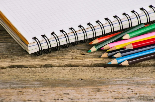 Zkontrolovat prázdné notebook s barevné tužky na dřevo pozadí — Stock fotografie