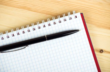 Ahşap masanın üzerinde kalem ve kalemle boş bir defter.