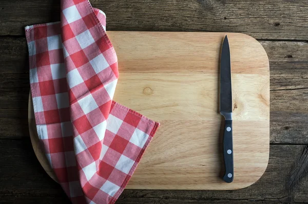 Papan pemotong kosong dengan pisau paring yang tajam dan serbet di atas meja kayu yang tertekan — Stok Foto