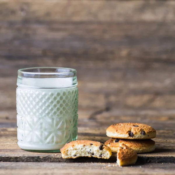 Leckere Plätzchen und ein Glas Milch auf rustikalem Holzgrund — Stockfoto