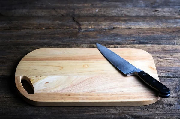 Placa de corte vazia com uma faca cortante afiada em uma mesa de madeira grunge angustiada em uma cozinha rústica, vista aérea com uma vinheta e copyspace — Fotografia de Stock