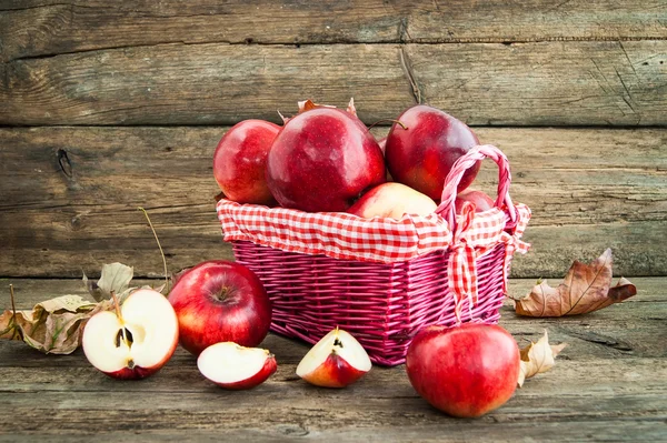 Červená jablka do koše na dřevěné pozadí — Stock fotografie