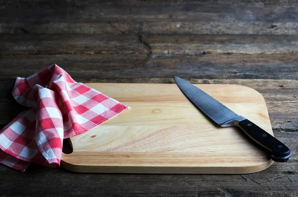 Leeres Schneidebrett mit scharfem Schälmesser und Serviette auf einem notleidenden Grunge-Holztisch — Stockfoto