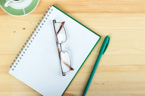 Glasses on notebook with pen and cup of coffee in wood table — Stock Photo, Image