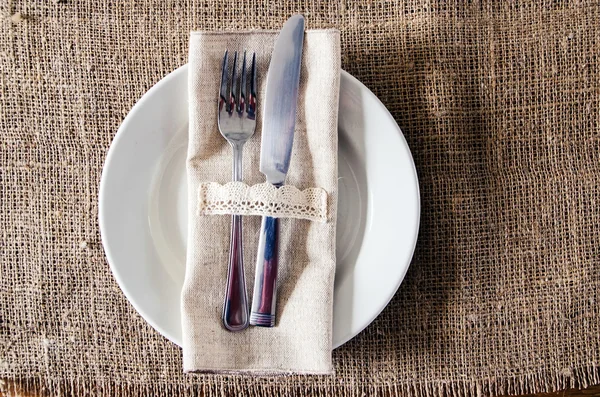 Prato vazio, faca e garfo em um guardanapo de serapilheira — Fotografia de Stock