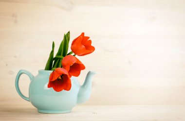 Spring tulips bouquet in teapot over wooden background