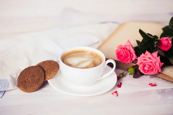 Filiżankę kawy na drewniany stół biały z plików cookie, róże i książek. — Zdjęcie stockowe