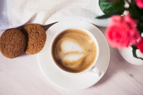 Tasse de café sur une table blanche en bois avec biscuits, roses et livres . — Photo