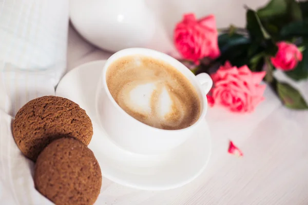 Tasse de café sur une table blanche en bois avec biscuits, roses et livres . — Photo