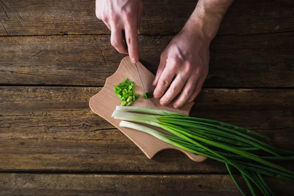 Man chopped green onion on the board. Wooden table — Stock Photo, Image