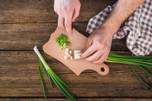 Mann hackt grüne Zwiebel auf dem Brett. Holztisch — Stockfoto