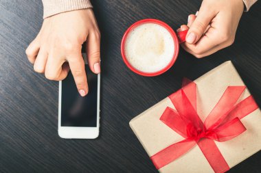 bir akıllı telefon ve kırmızı bir fincan kahve tutan kadın. Hediyelik kutu wi