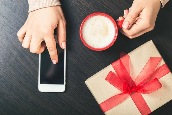 woman holding a smart phone and a red cup of coffee. gift box wi