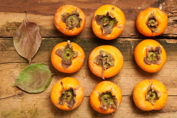 Persimmon resting on an old table — Stock Photo, Image