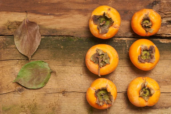 Persimmon resting on an old table — Stock Photo, Image