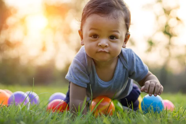 Bonito ásia bebê rastejando no o verde grama e colorido bola — Fotografia de Stock