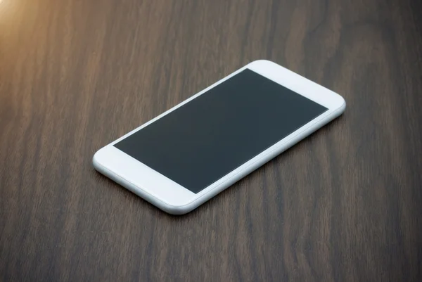 Teléfono inteligente con pantalla en blanco tumbado en la mesa de madera — Foto de Stock