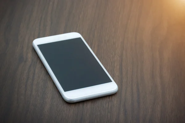 Smart phone con schermo bianco sdraiato sul tavolo di legno — Foto Stock