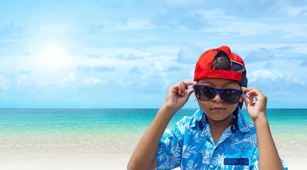 An Asian boys wear sunglasses and summer clothes on a bright summer sea background.