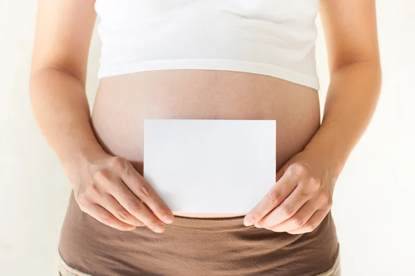 Mujer embarazada sosteniendo sus manos sobre el vientre y sosteniendo un blan — Foto de Stock
