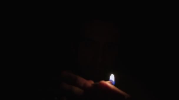 Um jovem no escuro ilumina os fósforos e ilumina o rosto — Vídeo de Stock