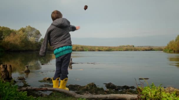 Gehandicapte jongen gooit een steen in het water. Langzame beweging — Stockvideo