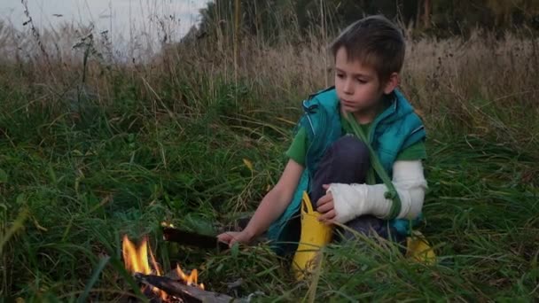 Blond chłopiec z bandażowaną ręką patrzy na ogień — Wideo stockowe