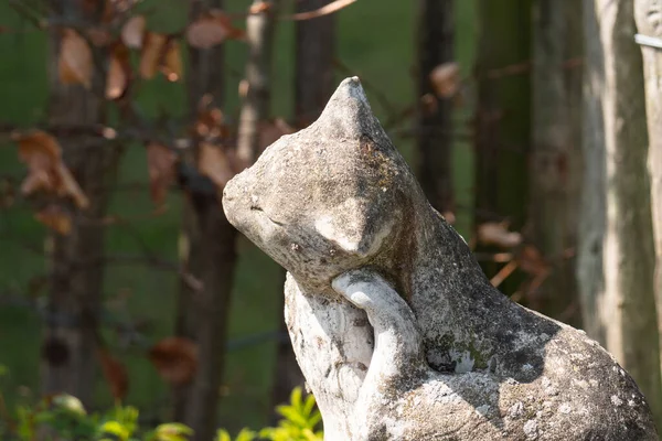 Close up of a concrete weathered statue of a cat scratching behind her ear