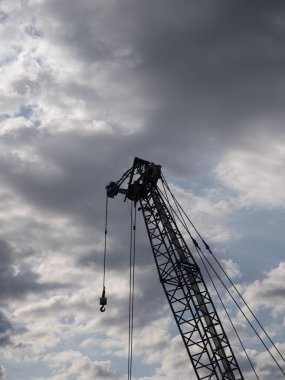 Arkaplan olarak mavi ve koyu bulutlu gökyüzü ile kancalı büyük bir vinç silueti