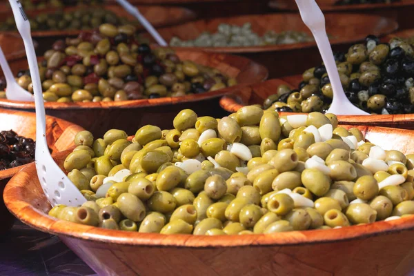 Brown dish with green olives in olive oil and white serving spoons in the bowls