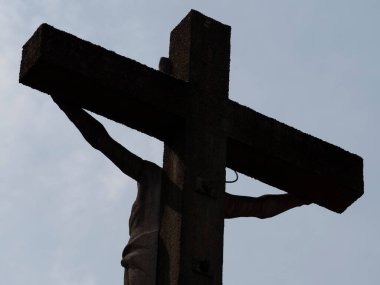 Büyük beton bir haçın arkasında gri mavi gökyüzü ve İsa Mesih 'in silueti.