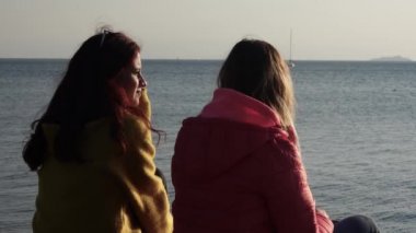 Öğleden sonra güneşinde deniz kenarında sohbet eden iki genç kadın. Şık kadınlar, güneşli bir sonbahar gününde deniz kıyısında günlük meselelerden bahsederler..